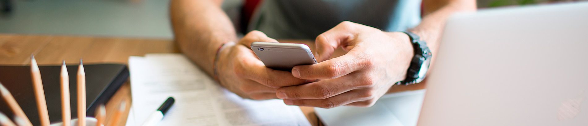 Foto das mãos de um homem apoiadas sobre uma mesa segurando um celular fazendo um pagamento instantâneo